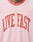 Close-up of a person in the LIVE FAST DIE YOUNG Live Fast Contrast Tee, a soft light pink shirt featuring LIVE FAST printed boldly in red capital letters across the chest.