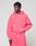 A person in a bright pink Basic Hooded Zip and matching sweatpants from LIVE FAST DIE YOUNG, featuring subtle branding, stands against a plain light gray background, gazing slightly to the side with one hand in their pocket.