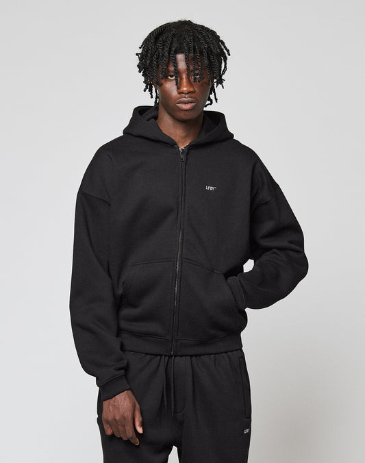 A person with short, curly hair wears the Basic Hooded Zip by LIVE FAST DIE YOUNG and matching black sweatpants, standing against a plain light gray background.