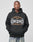 A person wears the Live Fast Tribal Hooded by LIVE FAST DIE YOUNG, a black oversized Baumwolle hoodie with LIVE FAST DIY BOWERY HARLEM, NY graphic text, standing against a light gray background with hands in the pockets.