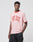 A man poses against a plain light background wearing the LIVE FAST DIE YOUNG Live Fast Contrast Tee—a light pink cotton T-shirt with bold red LIVE FAST print—and black shorts.