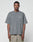 A man faces forward in an oversize fit, faded gray Basic +49 Chest Tee by LIVE FAST DIE YOUNG with a “+49.LiveFast” logo on the left chest and light brown mesh shorts, set against a plain white background.