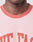 Close-up of a person wearing the LIVE FAST DIE YOUNG Live Fast Contrast Tee—light pink with raglan sleeves, darker pink collar, and partial red lettering—showing the bottom half of their face and neck.