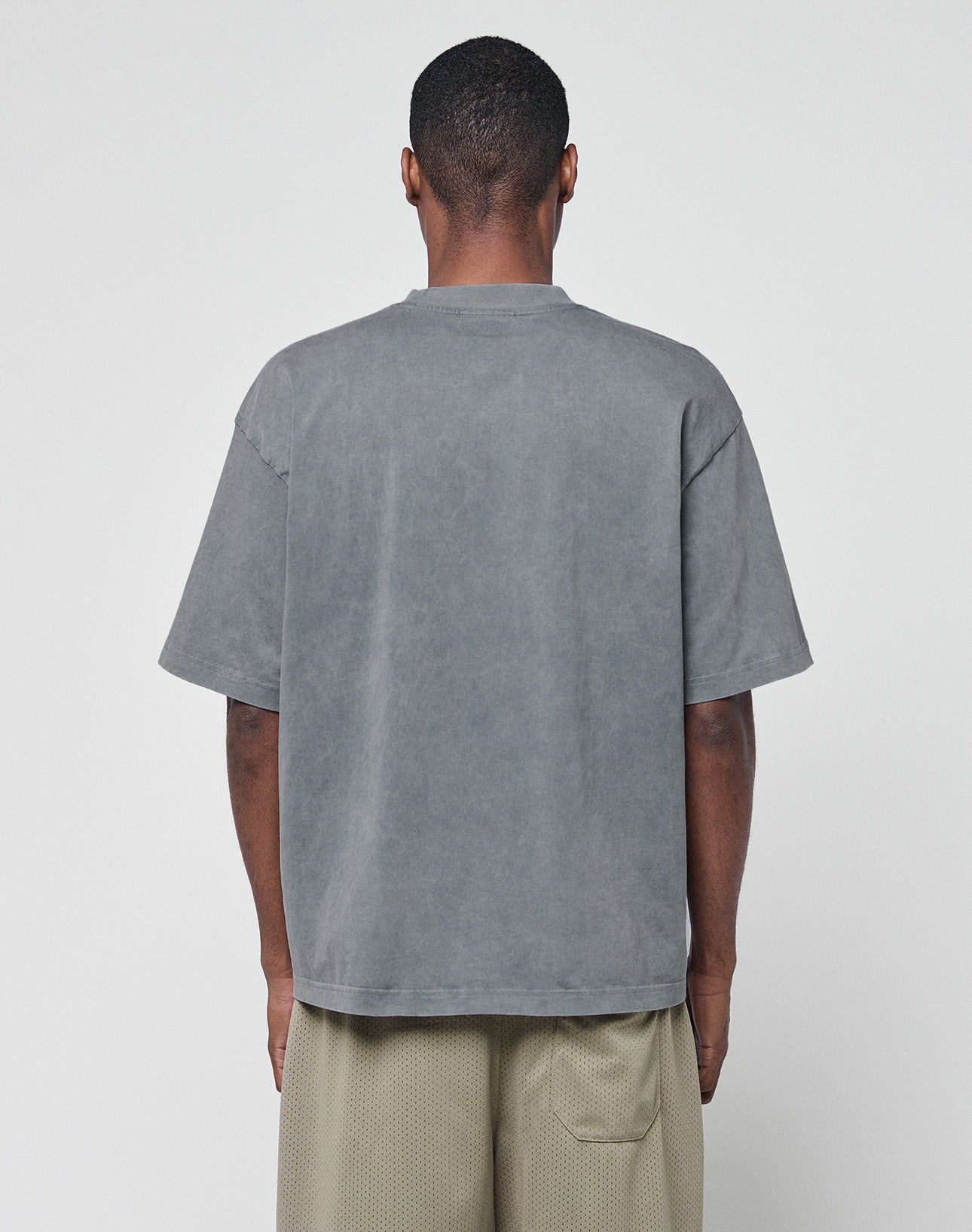 A person faces away from the camera, wearing a loose Basic +49 Chest Tee by LIVE FAST DIE YOUNG in faded gray and light beige mesh oversize shorts, set against a plain white background.