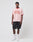 A young man faces forward, wearing the LIVE FAST DIE YOUNG Live Fast Contrast Tee in light pink with red trim and raglan sleeves, bold red LIVE FAST text, paired with black shorts, white socks, and sneakers against a grey background.