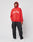 A person wears the LIVE FAST DIE YOUNG Live Fast Fractured Hooded red hoodie with doppellagige Kapuze and Live Fast text, black cargo pants, and white sneakers, standing against a plain light background.