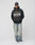 A man wears an oversize black Live Fast Tribal Hooded from LIVE FAST DIE YOUNG, featuring HARLEM, NY text, with faded blue jeans, white sneakers, and a black leather cap against a plain white background. Polyester/Baumwolle blend for comfort.