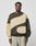 A man faces forward in a LIVE FAST DIE YOUNG LFDY Wavy Sweater, an oversized two-tone olive green and beige Baumwolle piece with curved panel designs, paired with light gray pants against a plain background.