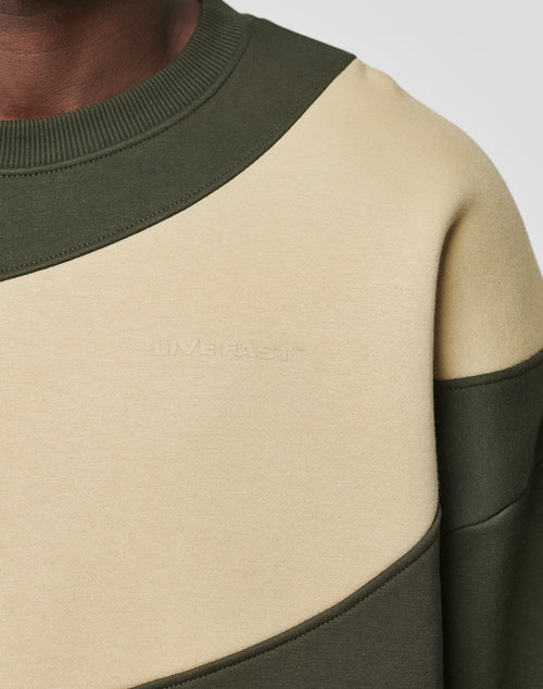 Close-up of a person wearing the LIVE FAST DIE YOUNG LFDY Wavy Sweater in olive green and beige, featuring a ribbed collar, oversized fit, faintly embossed LIMEFAS on the front, and crafted from soft cotton and polyester.