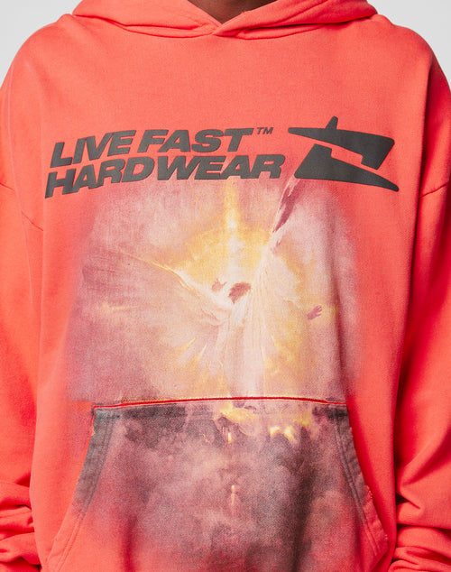 A person wearing the LIVE FAST DIE YOUNG LFDY Angel Hooded in coral, featuring bold black LIVE FAST HARDWEAR text, a stylized logo, faded abstract design with distress effect by the pocket, and an oversize fit for comfort.