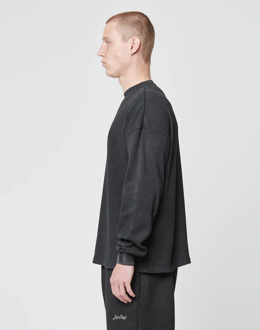 A man with short hair stands in profile against a plain white background, wearing LIVE FAST DIE YOUNGs Blank Waffle Longsleeve and matching black pants, both made from 100% Baumwolle.