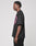 A young man with short twists stands in profile, wearing the LIVE FAST DIE YOUNG Live Fast Stallion Tee—an oversize black 100% Baumwolle T-shirt with a pink front print—paired with black pants, against a plain light gray background.