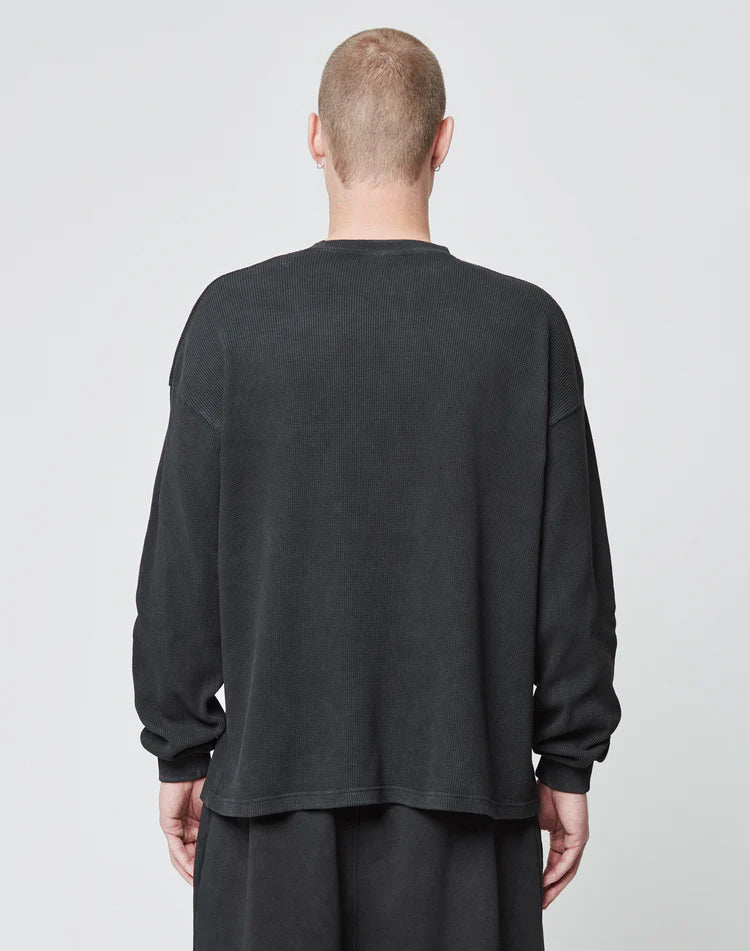 A person with short hair is seen from behind wearing the LIVE FAST DIE YOUNG Blank Waffle Longsleeve in an oversize fit and matching black 100% Baumwolle pants, standing against a plain light background.