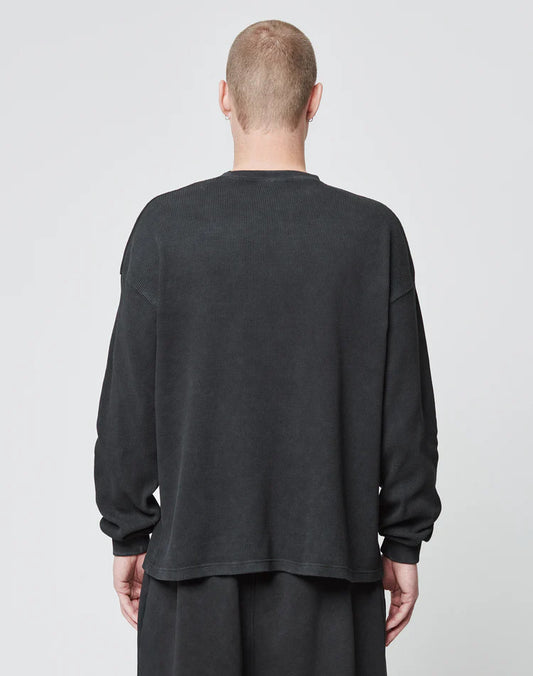 A person with short hair is seen from behind wearing the LIVE FAST DIE YOUNG Blank Waffle Longsleeve in an oversize fit and matching black 100% Baumwolle pants, standing against a plain light background.