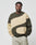A man in light gray pants stands with hands in pockets wearing the LIVE FAST DIE YOUNG LFDY Wavy Sweater—an oversized fit made from soft cotton and polyester, featuring bold olive green and beige curved color blocks. He has a neutral expression.