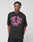 Someone wearing the Live Fast Stallion Tee by LIVE FAST DIE YOUNG, an oversize-fit black T-shirt featuring bold pink LIVE FAST text and a front print of three running animals, stands against a plain light background.