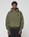 A person wears the LIVE FAST DIE YOUNG Basic 360 Hooded in olive green with topstitching and "LiveFast" on the chest, styled with black pants and standing against a plain light gray background, looking at the camera. The hoodie has an oversize fit.