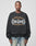 A person wears the LIVE FAST DIE YOUNG Live Fast Tribal Sweater, an oversize fit black cotton sweatshirt with a striking tribal graphic and LIVE FAST DIY HARLEM, NY on the front, paired with light blue jeans against a plain white background.