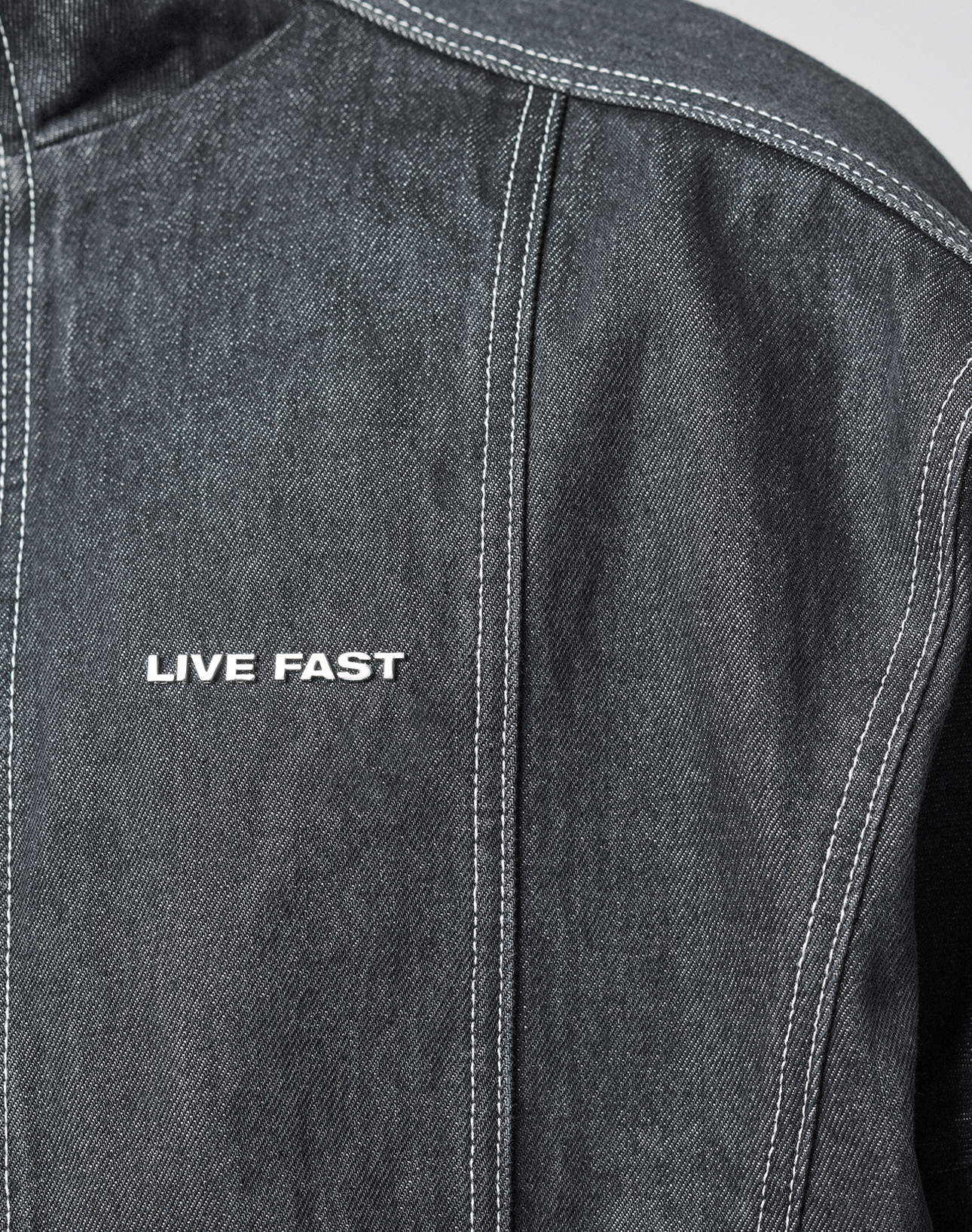 Close-up of the LFDY Denim Trackjacket by LIVE FAST DIE YOUNG: dark denim with Stehkragen, white stitching, and "LIVE FAST" embroidered on the front. Made from 100% Baumwolle with detailed craftsmanship.