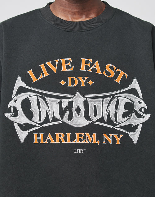 Someone wearing a Live Fast Tribal Sweater by LIVE FAST DIE YOUNG, featuring bold black fabric with orange and white LIVE FAST text in striking, stylized lettering.