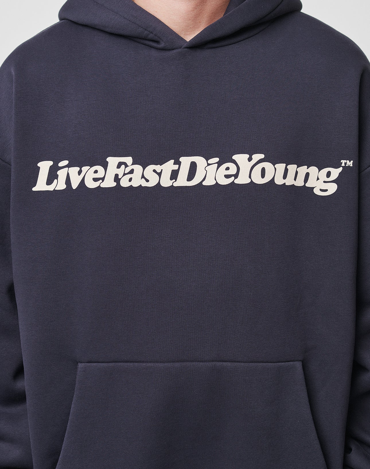 Someone wears the Basic Chest Hooded by LIVE FAST DIE YOUNG, a dark oversized hoodie with a bold white "LiveFastDieYoung" print on the chest.