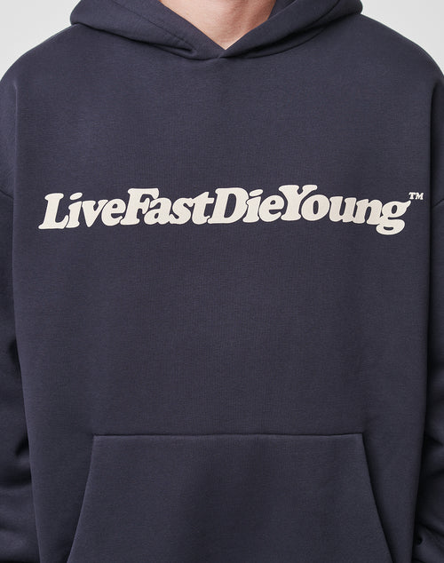Someone wears the Basic Chest Hooded by LIVE FAST DIE YOUNG, a dark oversized hoodie with a bold white "LiveFastDieYoung" print on the chest.