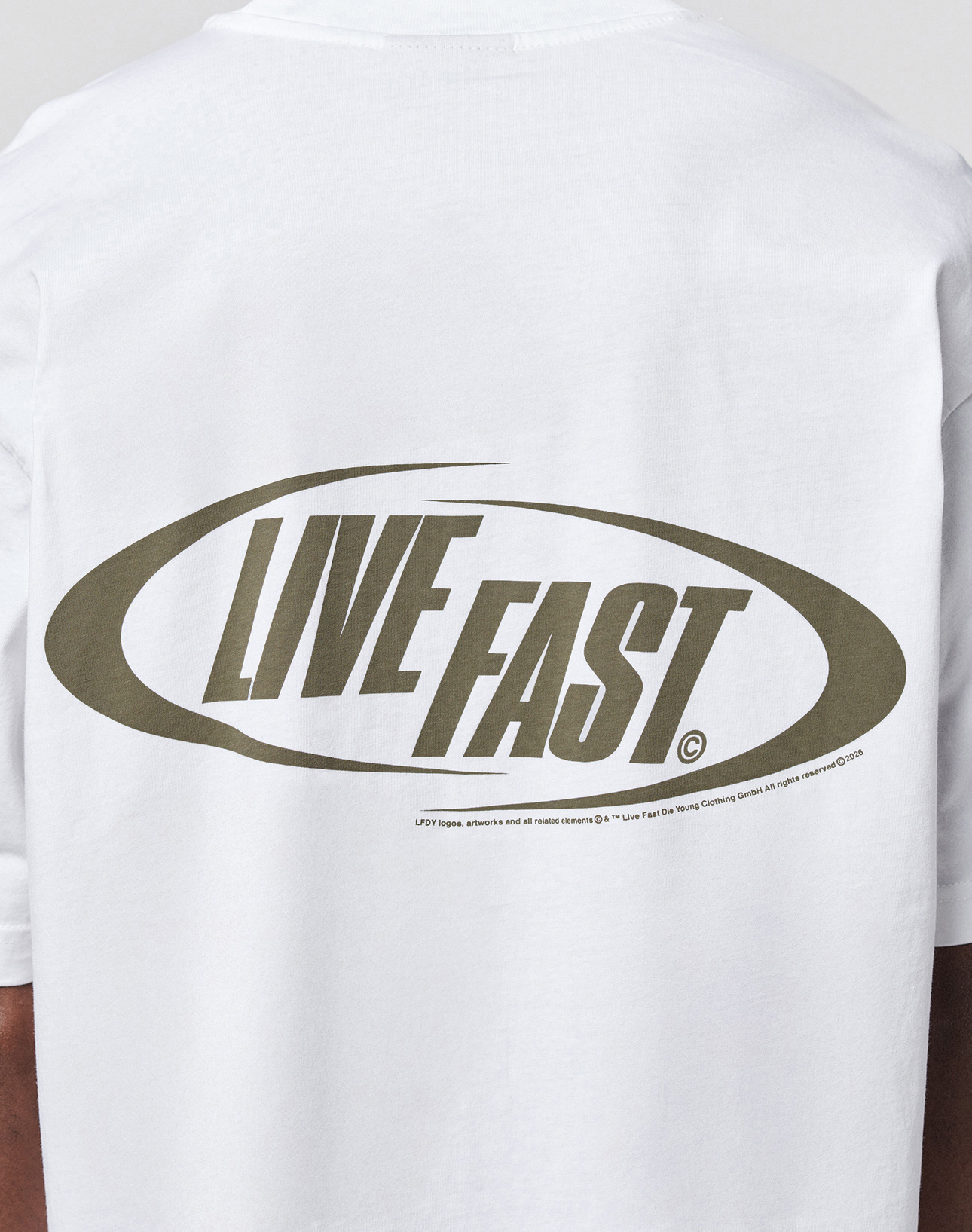 The LFDY Sphere Tee by LIVE FAST DIE YOUNG is a white, oversize cotton shirt with “LIVE FAST” in bold olive-green letters inside an oval on the back, front and back prints, plus small trademark and copyright details below the graphic.