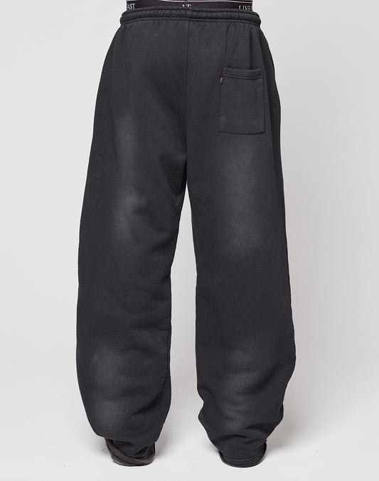 A person models the LIVE FAST DIE YOUNG Live Fast Rhinestone Jogger, featuring a wide fit, high waist, black color, and single front pocket. Their upper body is not visible as they stand against a plain white background.