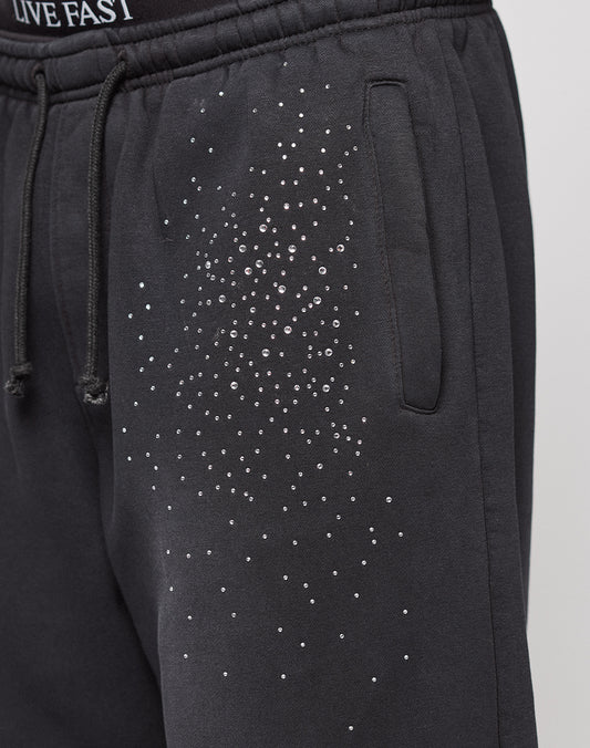 The Live Fast Rhinestone Jogger by LIVE FAST DIE YOUNG features black sweatpants with an elastic waistband, side pocket, rhinestone Muster on the upper thigh, partially visible "LIVE FAST" text, and a wide fit for comfort.