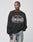 A person wears the Live Fast Tribal Sweater by LIVE FAST DIE YOUNG, an oversized black cotton-polyester sweatshirt with tan and white HARLEM, NY graphics, paired with light blue jeans against a simple light background.