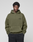 A young man with short curly hair models the LIVE FAST DIE YOUNG Basic 360 Hooded in olive green, featuring topstitching and an oversized fit, paired with black pants against a plain light gray background.