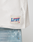 Close-up of a white LFDY Boxy Jersey by LIVE FAST DIE YOUNG with a label near the hem, styled with light blue jeans featuring white paint splatters.