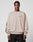 A man wears the LIVE FAST DIE YOUNG Live For It Sweater—a loose, beige 100% cotton sweatshirt with LIVE IT FAST on the chest and black sleeve text—in an oversize fit, standing against a plain background with a neutral expression.