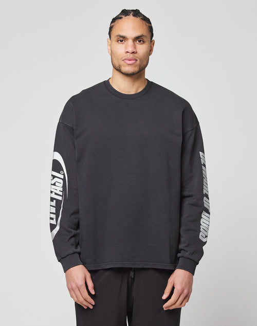 A man with braided hair wears the LFDY Canine Longsleeve by LIVE FAST DIE YOUNG, a loose black 100% Baumwolle sweatshirt with white sleeve text and reflektierender Druck, standing against a plain light gray background.