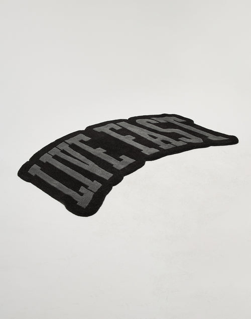 The Live Fast Carpet by LIVE FAST DIE YOUNG is a black rug featuring large gray LIVE FAST letters on a plain white background, made from 100% wool and easy to maintain with proper carpet care.