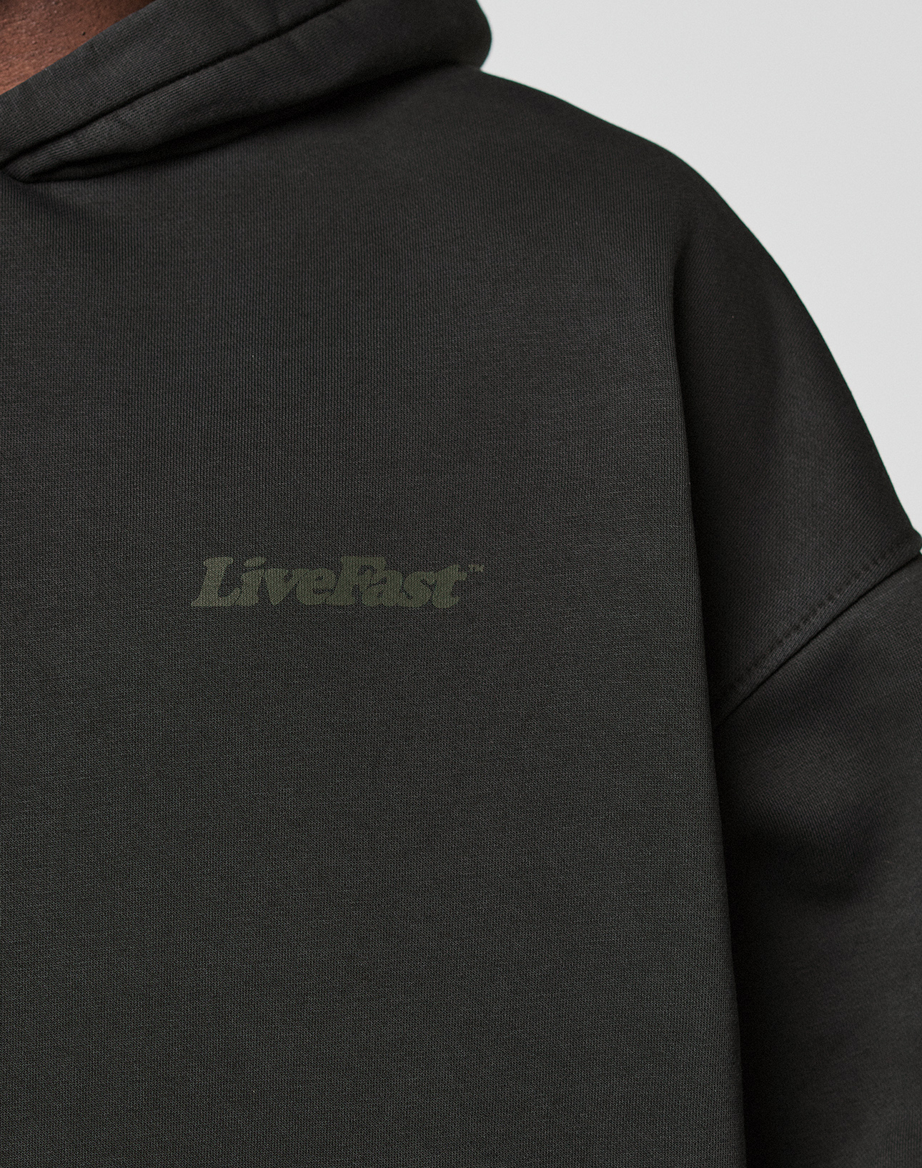 Close-up of the Basic 360 Hooded by LIVE FAST DIE YOUNG: an oversize fit black cotton sweatshirt with subtle "LiveFast" front print and additional print details on front and back. Soft, slightly textured fabric.