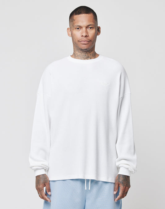A man with short hair and tattoos faces forward in an oversize LIVE FAST DIE YOUNG Basic Waffle Longsleeve (100% Baumwolle, white) and light blue mesh shorts, set against a plain light gray background.