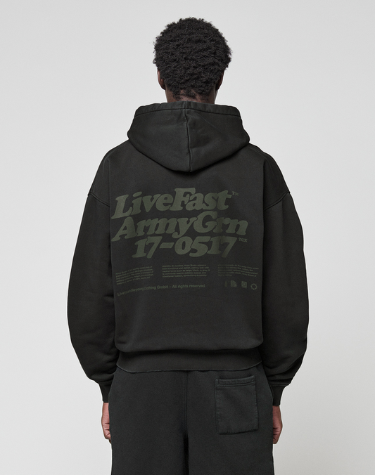 A person wearing the LIVE FAST DIE YOUNG Basic 360 Hooded black hoodie with the hood up, seen from behind. The back showcases large green "LiveFast ArmyGrn 17-0517" text and small writing—a stylish front and back print design.