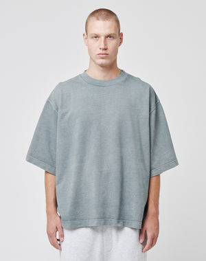 A young man with short blond hair stands against a plain background, wearing a faded gray Cropped Oversize Tee by LIVE FAST DIE YOUNG and light gray shorts. He faces forward with a neutral expression, highlighting an extreme oversize style.