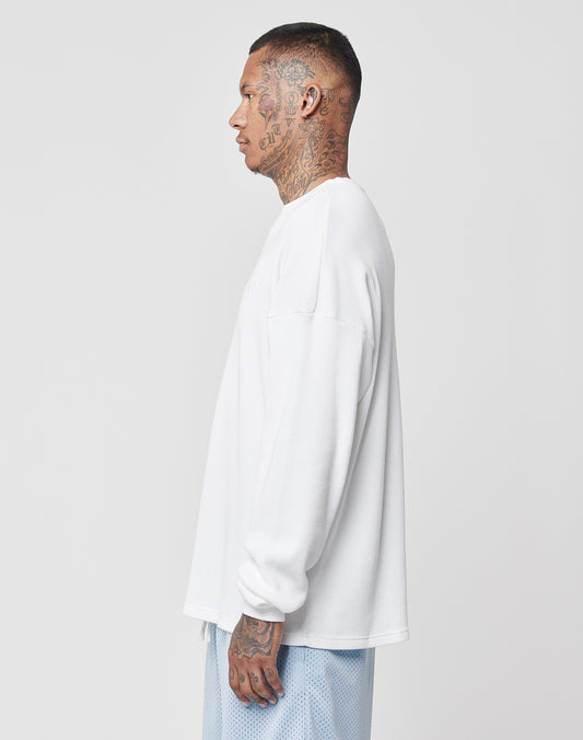 A tattooed man stands in profile, wearing a white LIVE FAST DIE YOUNG Basic Waffle Longsleeve and light blue shorts against a plain white background.