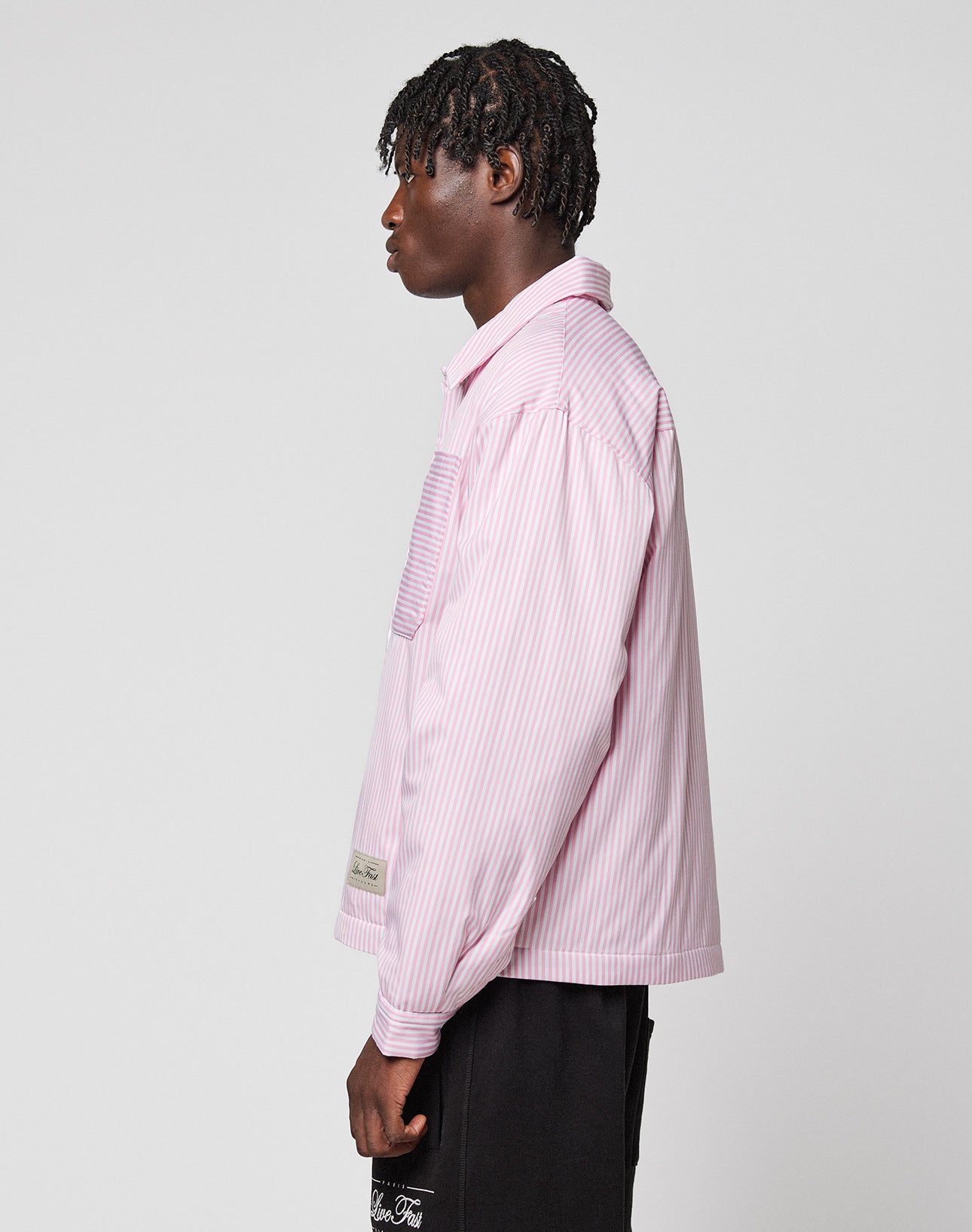 A person with short, textured hair stands in profile against a light gray background, wearing the LFDY Striped Padded Shirt by LIVE FAST DIE YOUNG and black shorts.