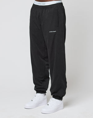 A person wearing LFDY Trackpants by LIVE FAST DIE YOUNG, featuring an elastic waistband and LIVE FAST text on the waistband and thigh, paired with white sneakers, stands against a plain white background.