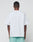 A person faces away from the camera, wearing the LIVE FAST DIE YOUNG Basic +49 Tee in white and mint green shorts, set against a plain light gray background.