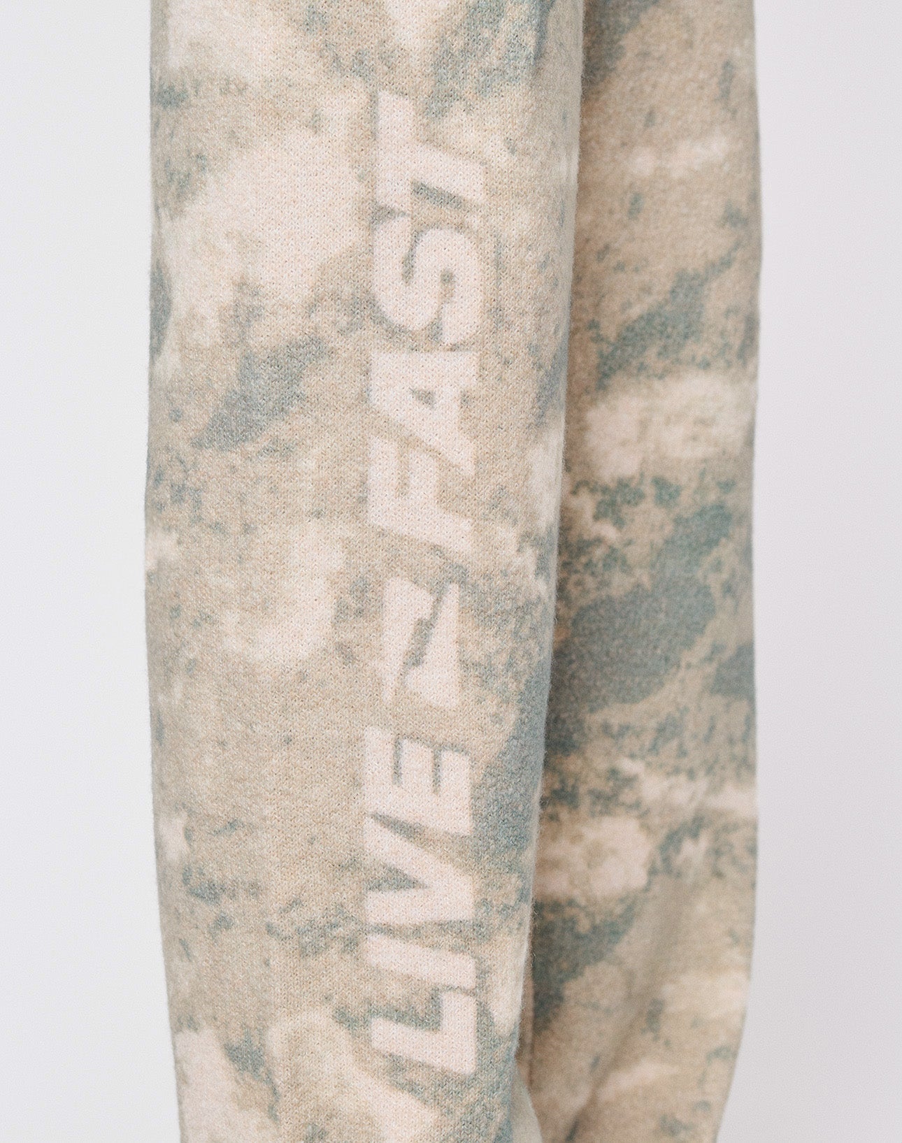 A close-up of the Live Fast Boucle Pants by LIVE FAST DIE YOUNG, featuring a beige and green tie-dye pattern with "LIVE FAST" printed vertically—ideal to pair with Wide Fit styles or pieces with a breiter Elastikbund for comfort.
