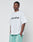 A man in a Basic +49 Tee by LIVE FAST DIE YOUNG, featuring an oversize fit and bold front print, pairs it with light green shorts while standing against a plain white background with his hands in his pockets.