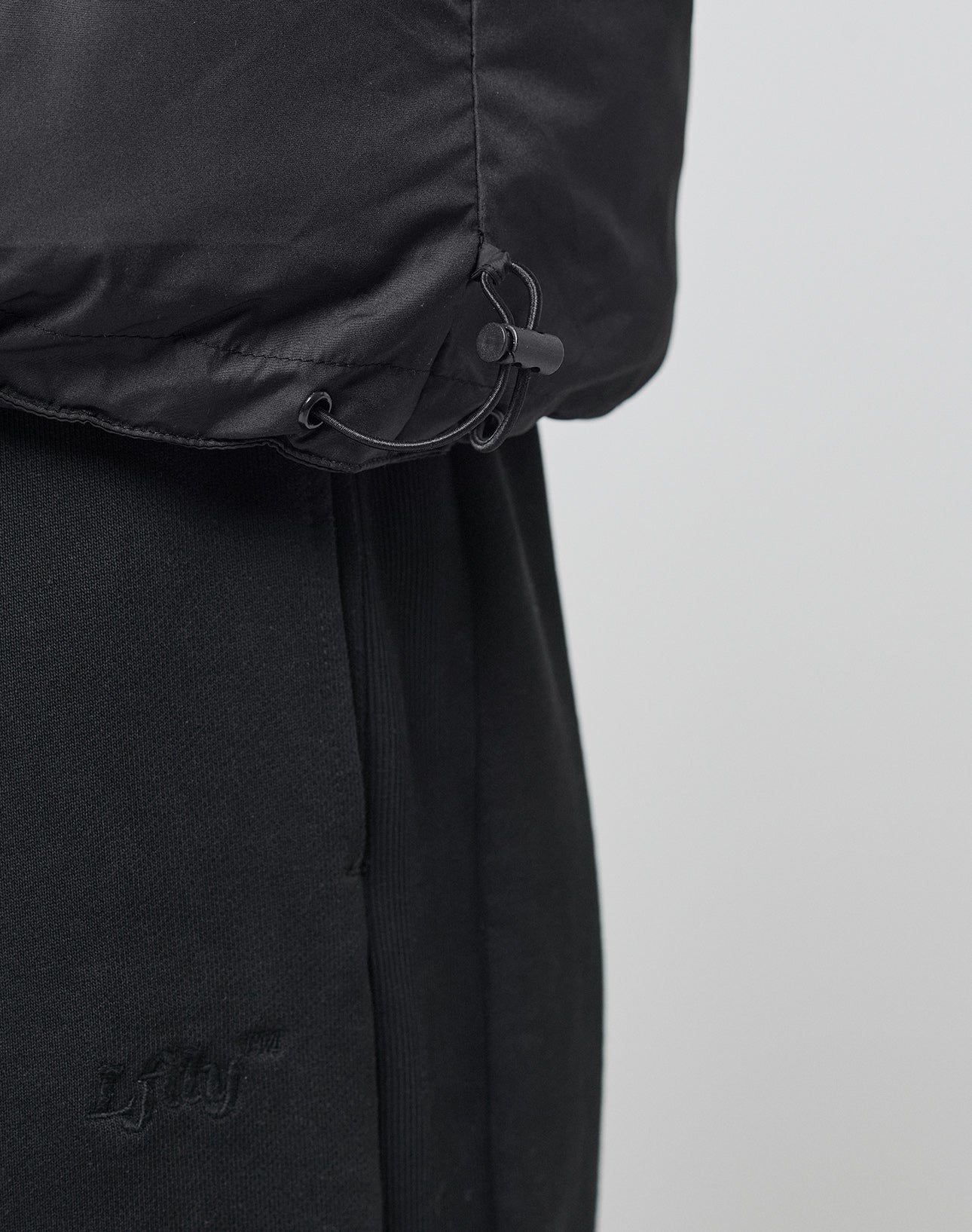 A close-up of the LFDY Puffer Jacket by LIVE FAST DIE YOUNG, featuring an oversize fit and adjustable drawstring hem, shown over black pants with the LFJU logo embroidered near the pocket.