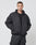 A person with short hair wears the LIVE FAST DIE YOUNG LFDY Puffer Jacket in an oversized fit with front logo stitching, paired with black pants, standing against a plain white background with hands in their pockets.