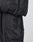 Close-up of a person in a black LIVE FAST DIE YOUNG LFDY Puffer Jacket with front logo stitching and black cargo pants featuring large pockets, highlighting the side and lower jacket details and upper section of the oversize fit pants.