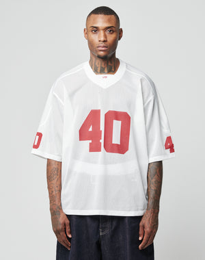 A tattooed man wears the LFDY Mesh Jersey by LIVE FAST DIE YOUNG—an oversized white mesh polyester top with a V-neck and red number 40 on front and sleeves—facing forward against a plain light gray background.