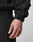 A close-up of a hand and wrist wearing the black Live Fast Nylon Jacket by LIVE FAST DIE YOUNG, featuring a textured finish, adjustable Velcro cuff strap, and side slit pockets. The background is plain and light-colored.